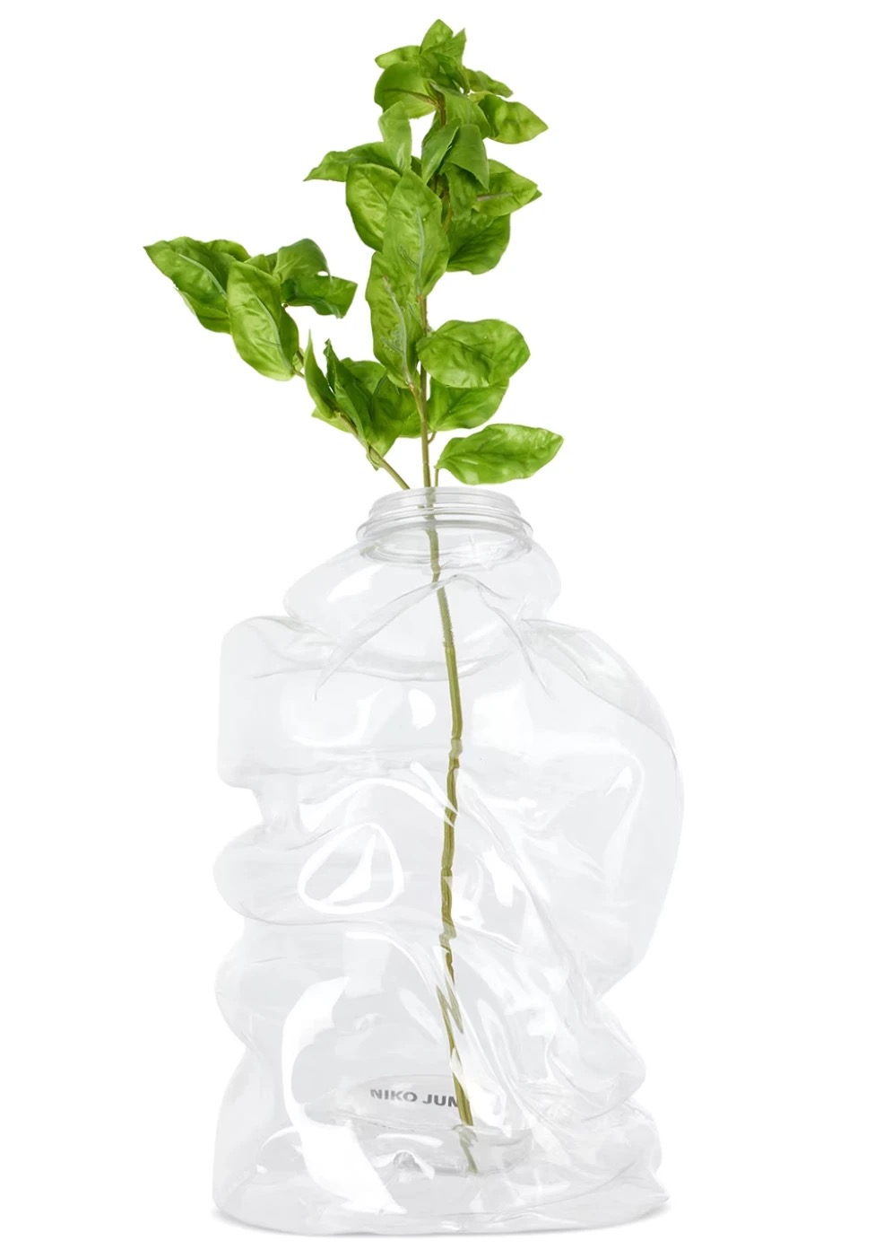 A vase made from a crushed, clear recycled bottle holding a basil sprig